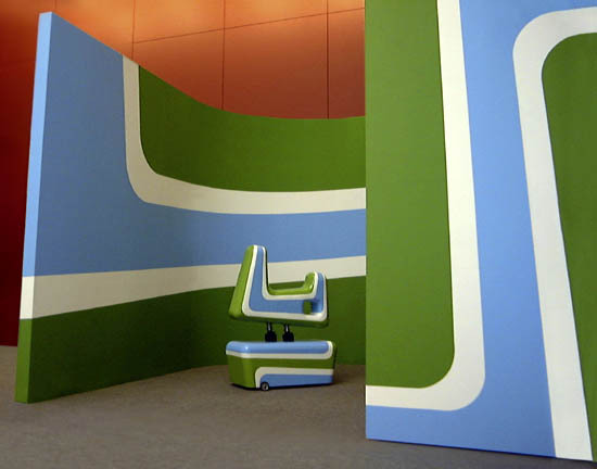 A green and blue sculptural structure next to an orange background.
