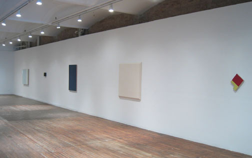 A series of colored objects hung on a long white wall.