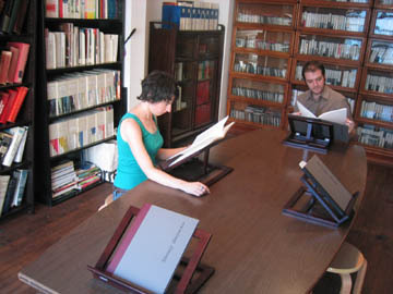 Two people in the a library space reading on book stands.