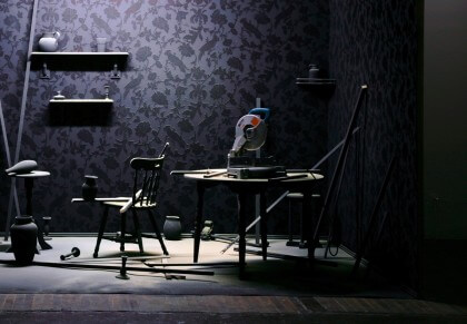 An installation view of Renggli's work, a dark room with various furniture and objects.
