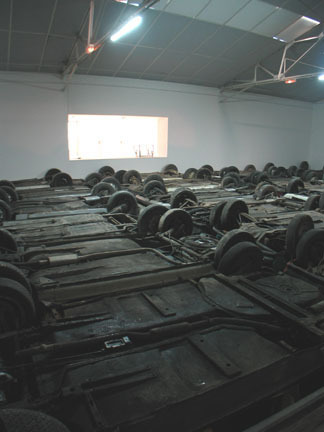 An installation view of the undercarriage of a series of cars placed on the floor of a galley.