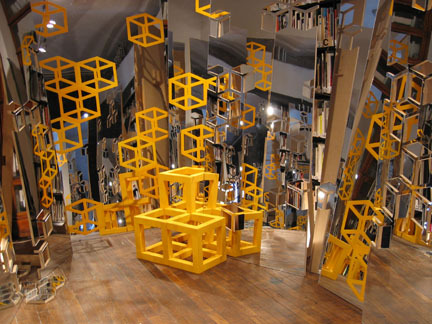 A room full of yellow box-shaped sculptures and mirrors.