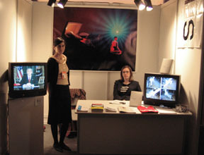 A image of two people in front of an art piece on a wall, and in between two TVs.