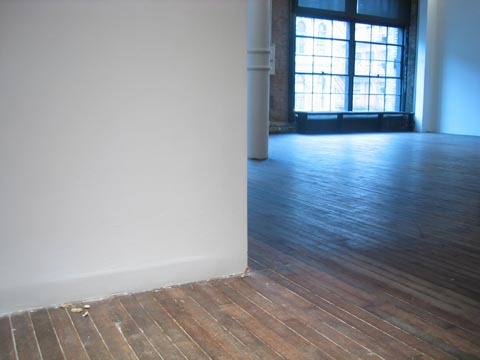 A white wall with wooden floors, and a big window in the back of the space.
