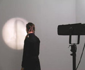 A person standing close to a wall, with their shadow being tracked by a light.