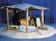 A close-up of a sculpture, with various items underneath a small roofed object.