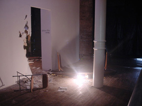 A dark room with a light laying on the floor, and the wall behind it crumbling.