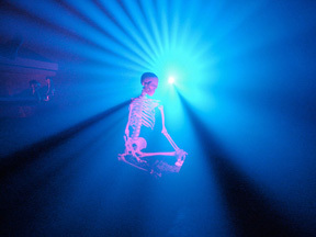 A skeleton floating the air in front of a big blue light.