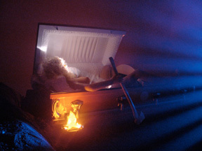A blue light cascades over a casket with a person sticking out.