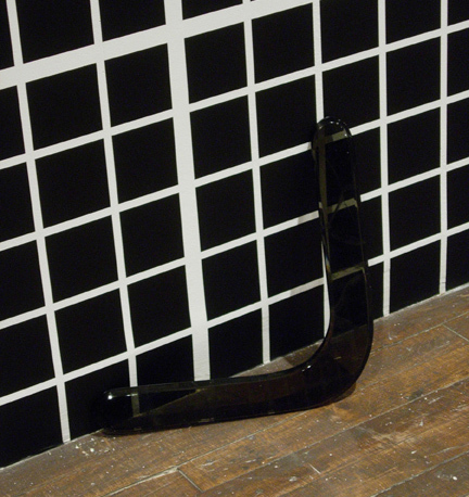 A black and white squared wall a small black sculpture on the ground.