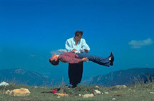 A person deviating next to another standing person, with the backdrop of clear blue skies and mountain tops.