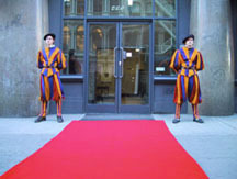 Two guards dressed in striped uniforms standing outside a building next to a long red carpet.
