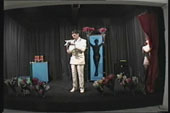 An image of a person standing on a black stage reading off a piece of paper with a silhouette of a female body behind them.