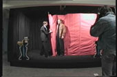 An image of a person standing on a black stage moving a red curtain around another person.