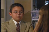 A close-up of a young child with glasses talking towards another person.
