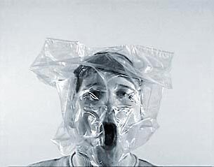 A black and white photo of a person with a bag over their head with the air sucked out and tight against their  face.