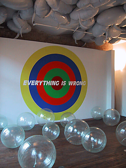 A room with balloons on the ceiling, wall art in the center, and round clear balls along the floor.