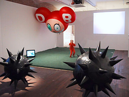 A closer view of the various sculptural and video installations in the gallery with a person standing in the middle.