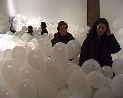 A few people standing in a room completely filled with white balloons.